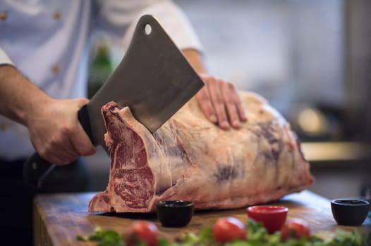 chef using ax while cutting big piece of beef  on wooden board in restaurant kitchen