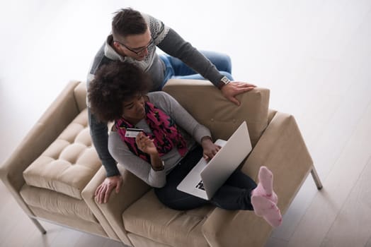 Happy young multiethnic couple shopping online through laptop using credit card at home