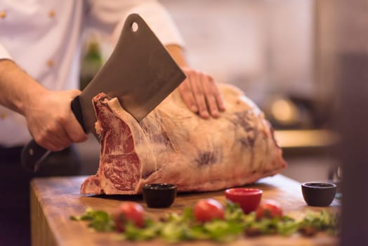 chef using ax while cutting big piece of beef  on wooden board in restaurant kitchen