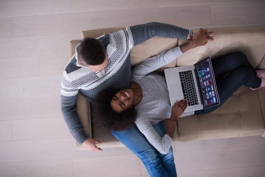Young multiethnic couple relaxes in the luxury living room, using a laptop computer top view