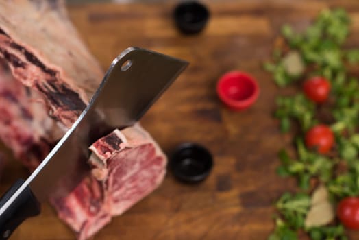 chef using ax while cutting big piece of beef  on wooden board in restaurant kitchen