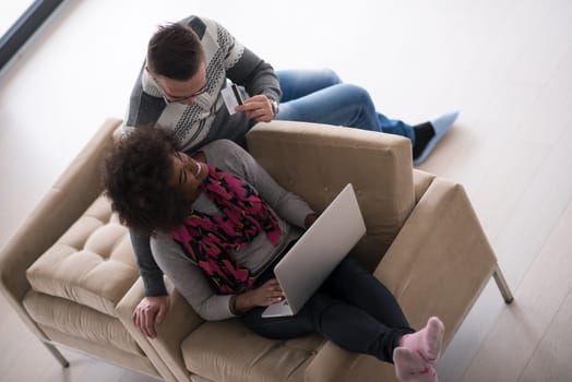 Happy young multiethnic couple shopping online through laptop using credit card at home