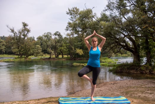 healthy woman relaxing while meditating and doing yoga exercise in the beautiful nature on the bank of the river