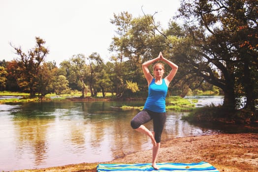 healthy woman relaxing while meditating and doing yoga exercise in the beautiful nature on the bank of the river
