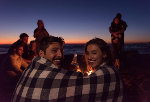 Young Couple enjoying with friends Around Campfire on The Beach At sunset drinking beer