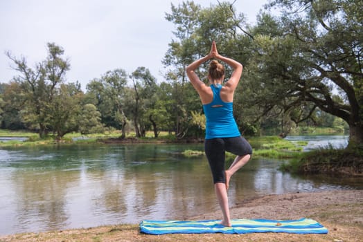 healthy woman relaxing while meditating and doing yoga exercise in the beautiful nature on the bank of the river
