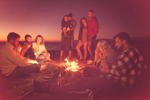 Young Couple enjoying with friends Around Campfire on The Beach At sunset drinking beer