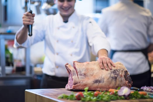 chef using ax while cutting big piece of beef  on wooden board in restaurant kitchen