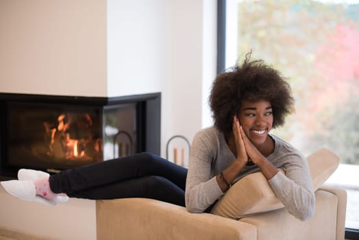 Young beautiful african american woman relaxing on chair in front of fireplace at autumn day