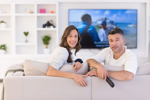 Young couple on the sofa watching television together in their luxury home