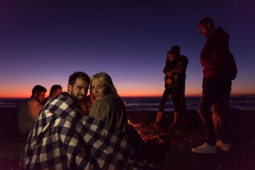 Young Couple enjoying with friends Around Campfire on The Beach At sunset drinking beer
