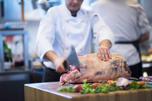 chef using ax while cutting big piece of beef  on wooden board in restaurant kitchen