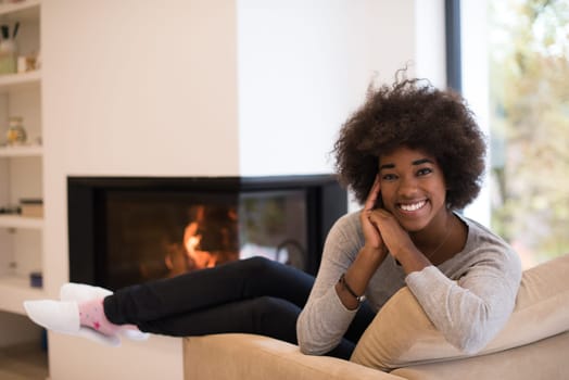 Young beautiful african american woman relaxing on chair in front of fireplace at autumn day