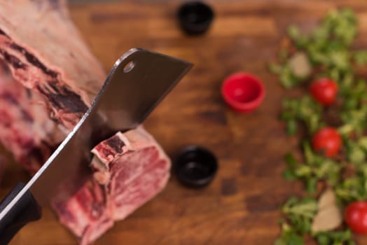 chef using ax while cutting big piece of beef  on wooden board in restaurant kitchen