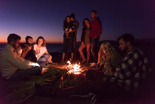 Young Couple enjoying with friends Around Campfire on The Beach At sunset drinking beer