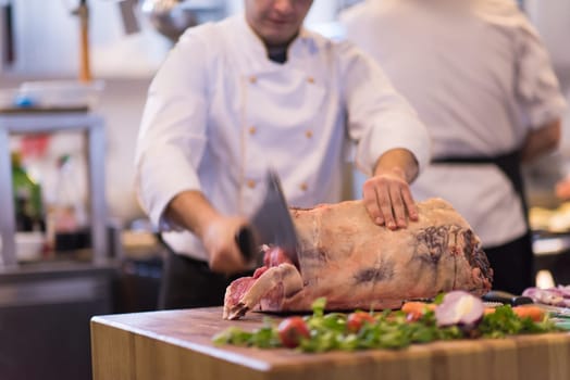 chef using ax while cutting big piece of beef  on wooden board in restaurant kitchen