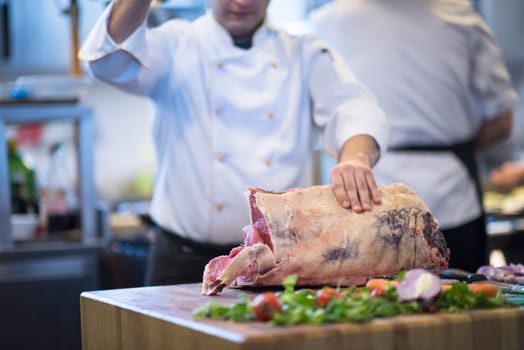 chef using ax while cutting big piece of beef  on wooden board in restaurant kitchen