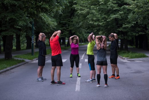 healthy runners team warming up and stretching in city park before morning training