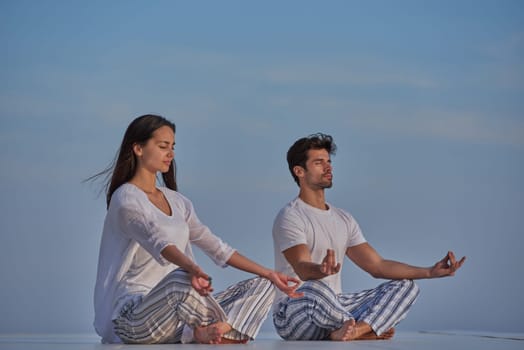 young couple practicing yoga at sunset in modern home terace with ocean and sunset in background