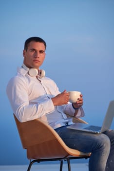 handsome young man relaxing and working on laptop computer at home balcony while looking sunset