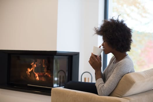 Happy joyful african american woman drinking cup of coffee relaxing at fireplace. Young black girl with hot beverage heating warming up. autumn at home.