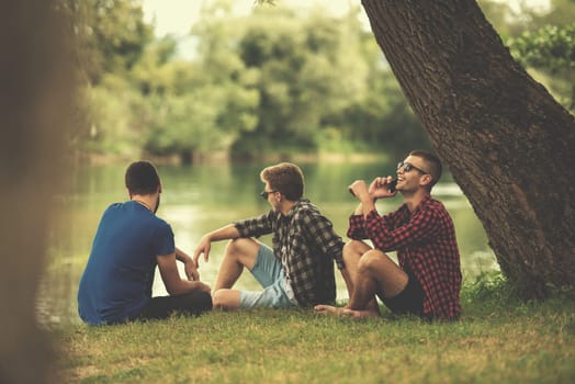 Group of young  men enjoying the nature sitting on the bank of the river