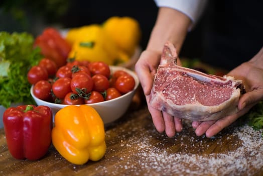Master Chef holding juicy slice of raw steak with vegetables around on a wooden table