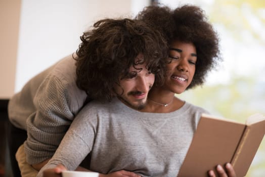 Young beautiful multiethnic couple hugging in front of fireplace at home when reading a book at autumn day