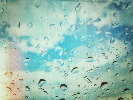 Water drops on window with blue cloudy sky behind