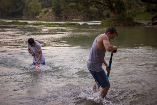young men having fun with water guns while splashing  each other during sunset on the river