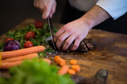 closeup of Chef hands in hotel or restaurant kitchen preparing beef steak with vegetable decoration