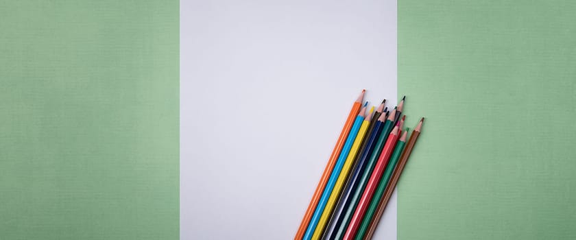 A blank white sheet and colored pencils for drawing on a plain textured background with space for copying and lettering. Layout, mockup free space.