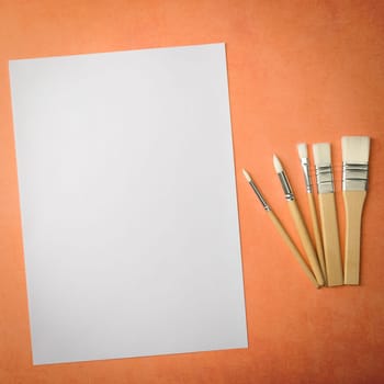 A clean white sheet and brushes on a textured background with space to copy. Layout, mockup space for text and drawing.