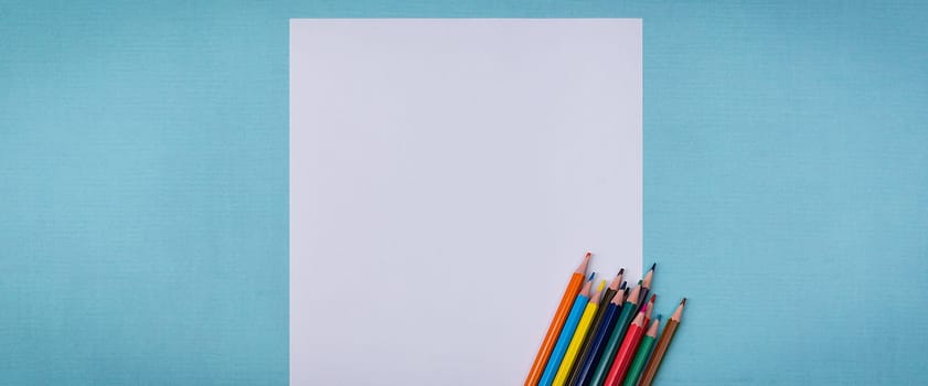 A blank white sheet and colored pencils for drawing on a plain textured background with space for copying and lettering. Layout, mockup free space.