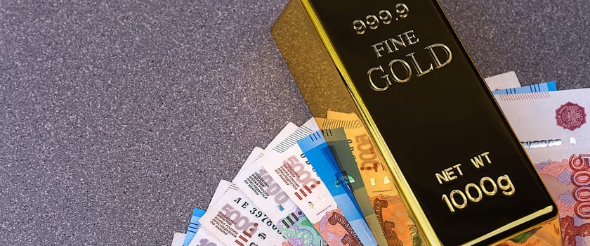 Gold bullion ingot and Russian ruble banknotes. The banknotes are spread out in a fan and pinned down with an ingot of gold.