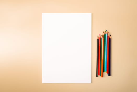 A blank white sheet and colored pencils for drawing on a plain textured background with space for copying and lettering. Layout, mockup free space.