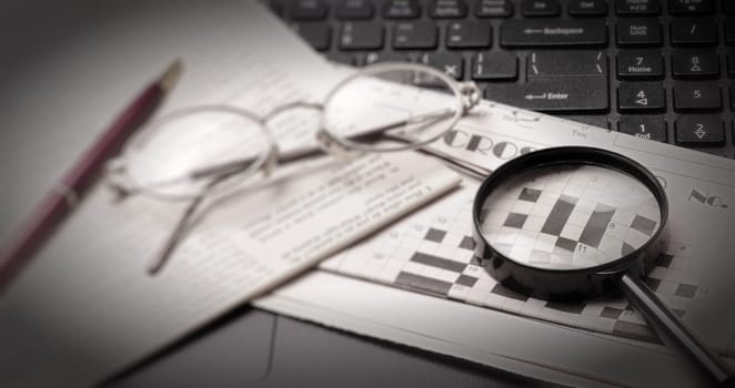 The glasses and old newspaper lying on the black open laptop. Selective focus