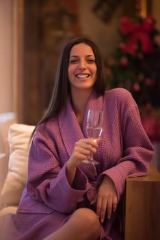 people, and relaxation concept   beautiful young woman in bath robe drinking champagne at spa over holidays lights background