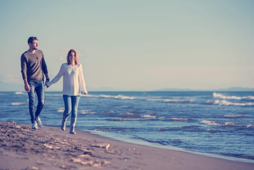 Young couple having fun walking and hugging on beach during autumn sunny day