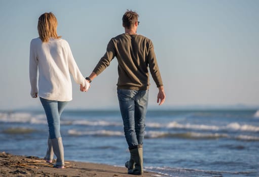 Young couple having fun walking and hugging on beach during autumn sunny day