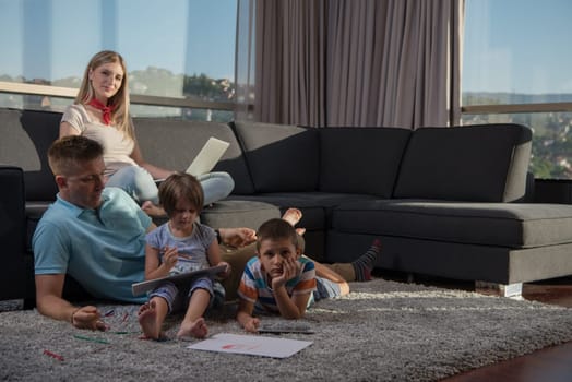 Happy Young Family Playing Together at home on the floor using a laptop computer and a children's drawing set