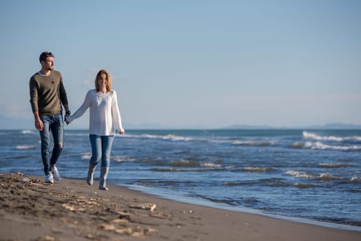 Young couple having fun walking and hugging on beach during autumn sunny day