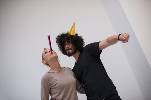 Young happy couple in party hats blowing in whistle isolated on a white background
