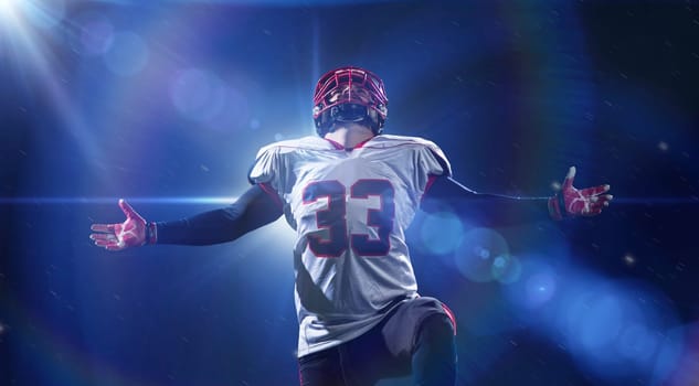 american football player celebrating after scoring a touchdown on the field of big modern stadium with lights and flares at night