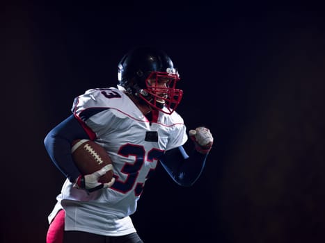 American football player holding ball while running on field at night