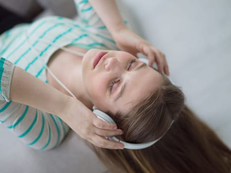 Young beautiful girl enjoying music through headphones, laying on sofa at home