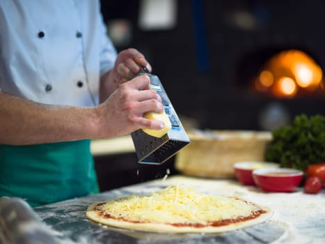 chef sprinkling cheese over fresh pizza dough on kitchen table