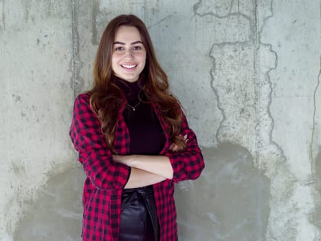 portrait of young successful smiling casual businesswoman standing in front of a concrete wall at new startup office
