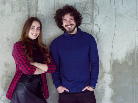 portrait of young successful smiling casual business couple standing in front of a concrete wall at new startup office