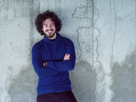 portrait of young successful smiling casual businessman standing in front of a concrete wall at new startup office